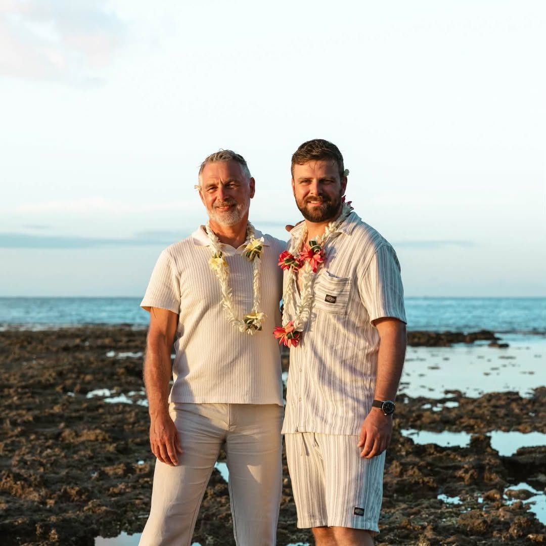 Couple de deux hommes en tenue blanche et colliers de fleurs sur le platier